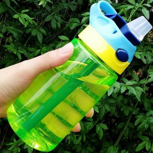 Botella antigoteo de 480 ml con tapa y pajita en verde, amarillo y azul delante de un árbol