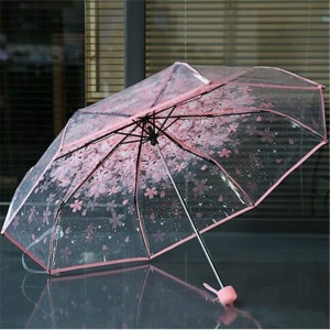 Paraguas transparente de flores para niños con borde rosa sobre una mesa delante de una ventana con las cortinas cerradas