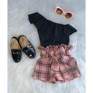 Pantalones cortos de cuadros rosas con camisa negra, gafas de sol rosas y zapatos negros brillantes sobre una alfombra blanca