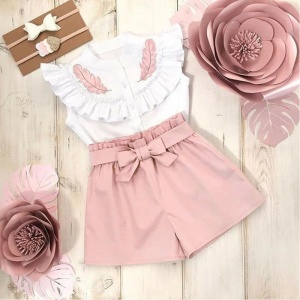 Pantalones cortos de color liso con una camiseta de niña rosa y blanca con plantas rosas a los lados y un fondo de madera