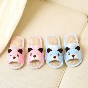 Pantuflas infantiles de oso a rayas rosas y azules sobre una alfombra beige junto a una cama