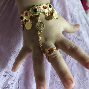 Pulsera y anillo unidos por una cadena para niña en mano de niño con falda blanca