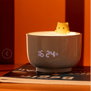 Luz nocturna en forma de taza de té con despertador con un gato sobre una revista y fondo naranja