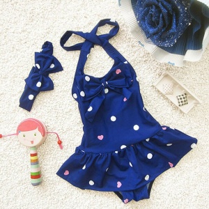 Traje de baño de una pieza para niña con diadema azul con lunares blancos y una muñeca a su lado sobre una alfombra blanca
