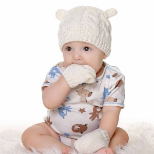 Conjunto de gorro y manoplas de invierno para bebé de color blanco con bebé con la mano en la boca y ropa blanca estampada