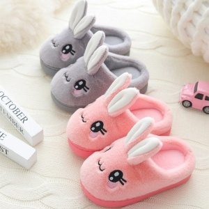 Zapatillas con orejas de conejo grises y rosas sobre alfombra blanca con ojos negros