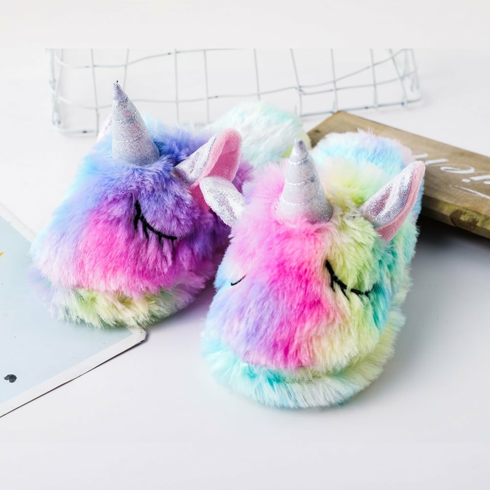 Zapatillas de unicornio arco iris para niños sobre una mesa blanca con suave pelaje