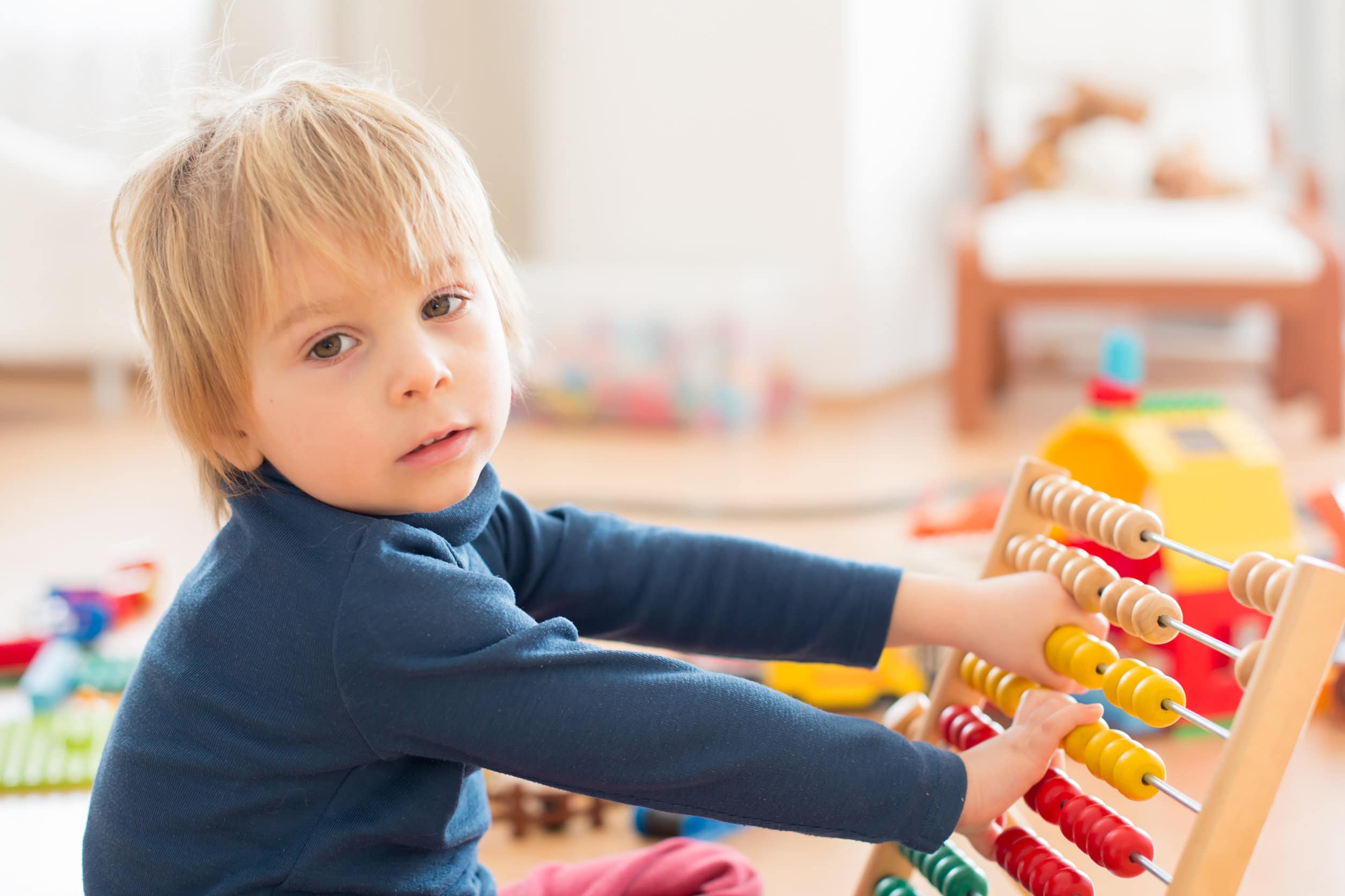 Un niño con el pelo rubio medio largo y un jersey azul jugando con un ábaco de colores para aprender a contar