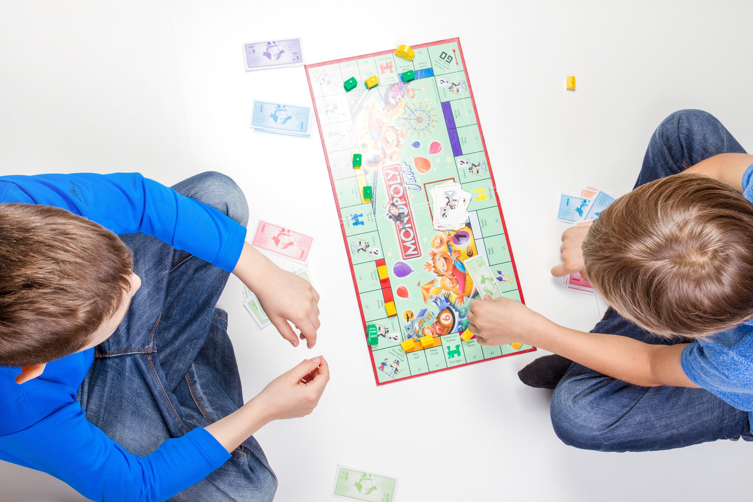 Dos niños pequeños jugando al monopoly, uno con un jersey azul y el otro con una camiseta azul