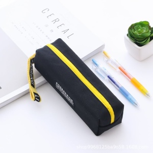 Estuche rectangular con tirador negro y amarillo sobre una mesa con cuaderno y bolígrafos y una planta
