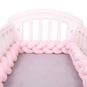 Tour de lit rose tresse dans un lit de bebe blanc avec draps gris