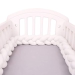 Tour de lit tressé blanc dans un lit de bébé blanc avec draps en gris
