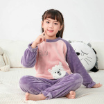 Pijama de franela polar con un bonito estampado para niños en morado y rosa sobre una niña en una alfombra blanca con un cojín en la espalda