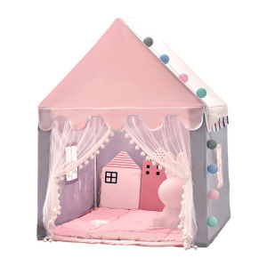 Tipi infantil con forma de casita rosa, con la parte delantera abierta y dos cortinas colgando a los lados. Hay pequeñas ventanas en los laterales. Dentro, hay un suelo acolchado rosa y cojines rosas.