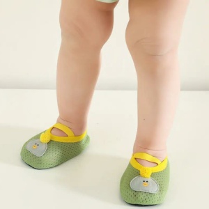 un bebé está de pie con sólo sus piernas visibles, llevando unos pequeños patucos verdes, suaves y transpirables